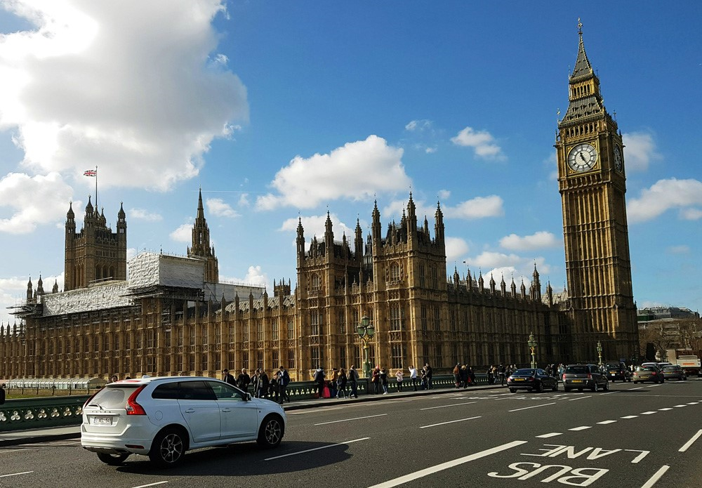 A car drives across Westminster Bridge towards Big Ben and the Houses of Parliament on a bright day